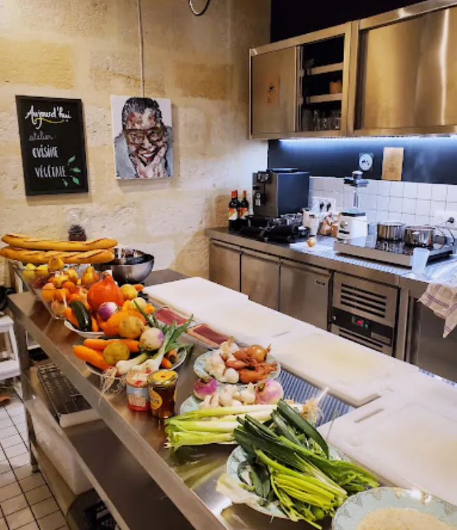 View of a Bordeaux kitchen featuring a central island displaying fresh fruits and vegetables including carrots, celery, oranges and local produce, with modern kitchen equipment in the background