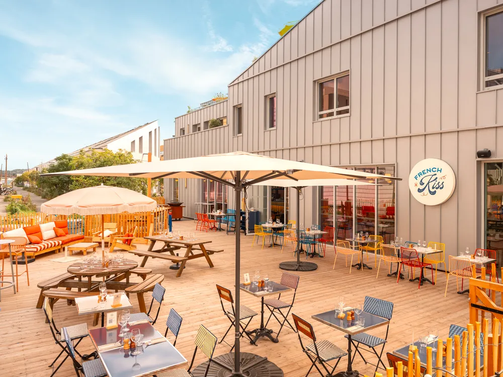 Sunny outdoor terrace of a restaurant featuring colorful chairs, tables, umbrellas, and modern building architecture in Bordeaux