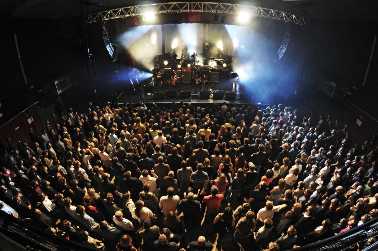 Overhead view of a packed concert hall with a dense crowd facing an illuminated stage with blue and white spotlights at the Krakatoa venue in Mérignac, Bordeaux.