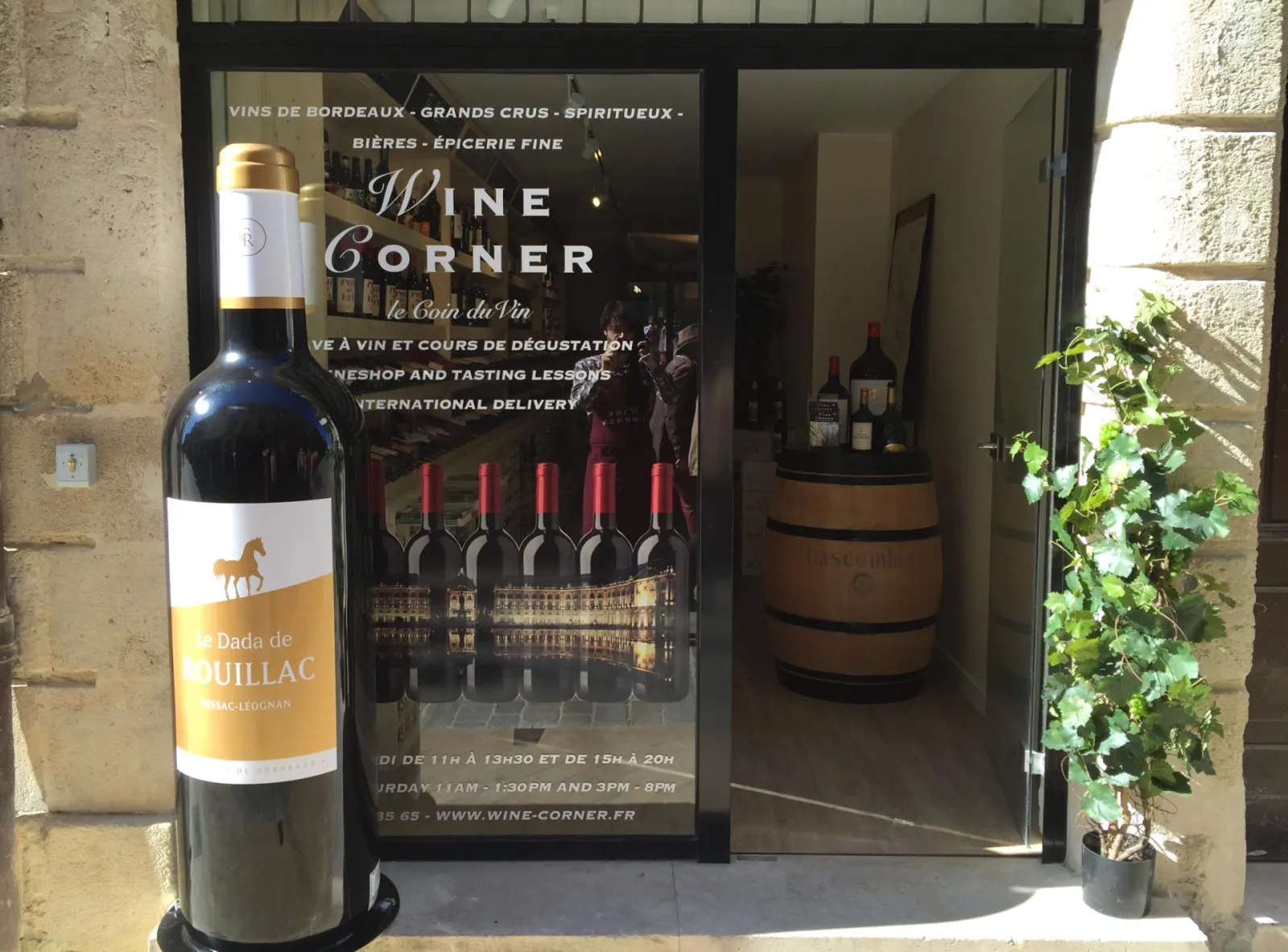 Wine Corner storefront in Bordeaux featuring a large bottle of Dada de Pauillac wine display and wine barrels inside the shop