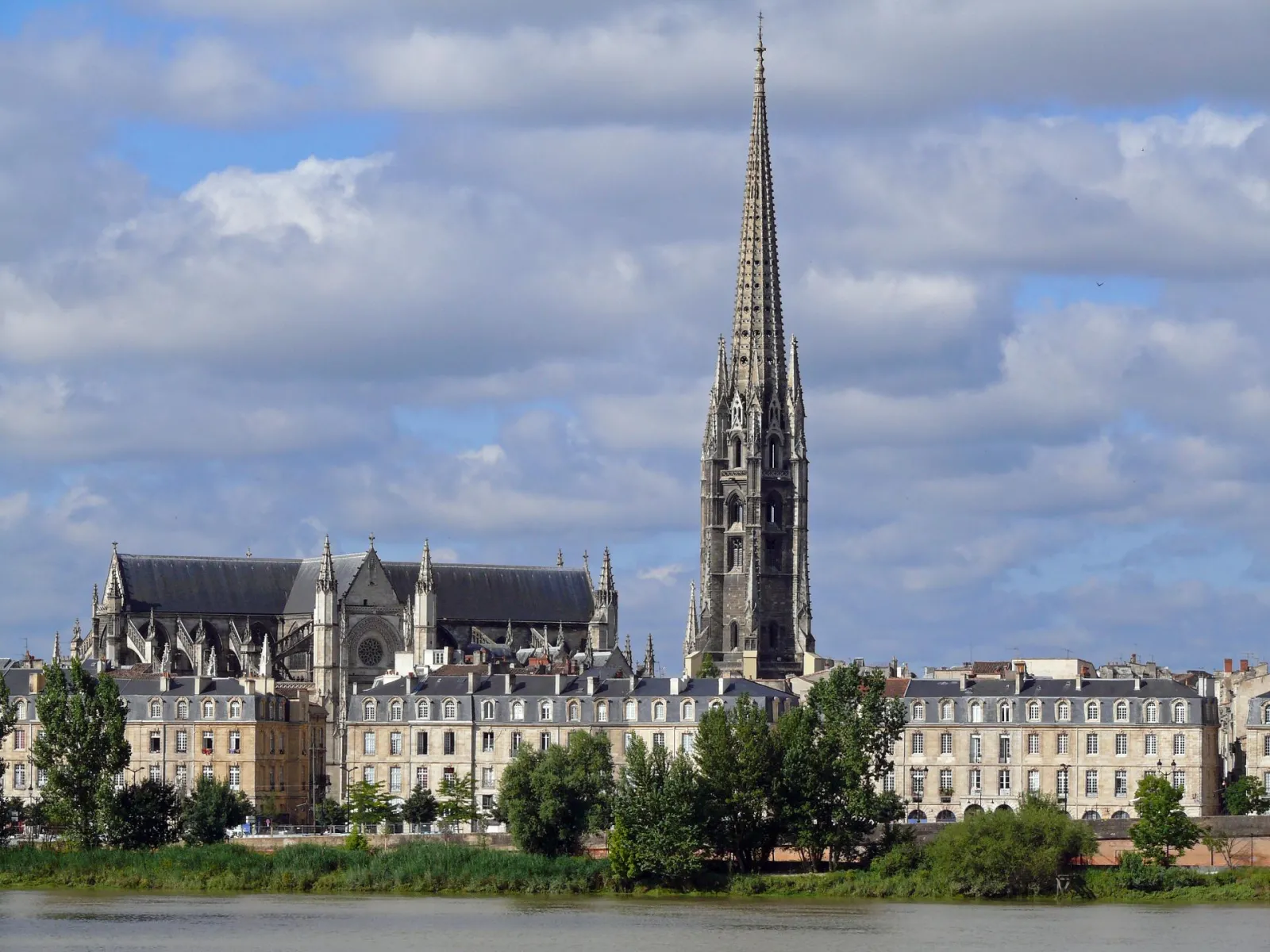 The Spire of Saint-Michael in Bordeaux with its tall Gothic bell tower rising above Haussmann-style buildings along the Garonne River