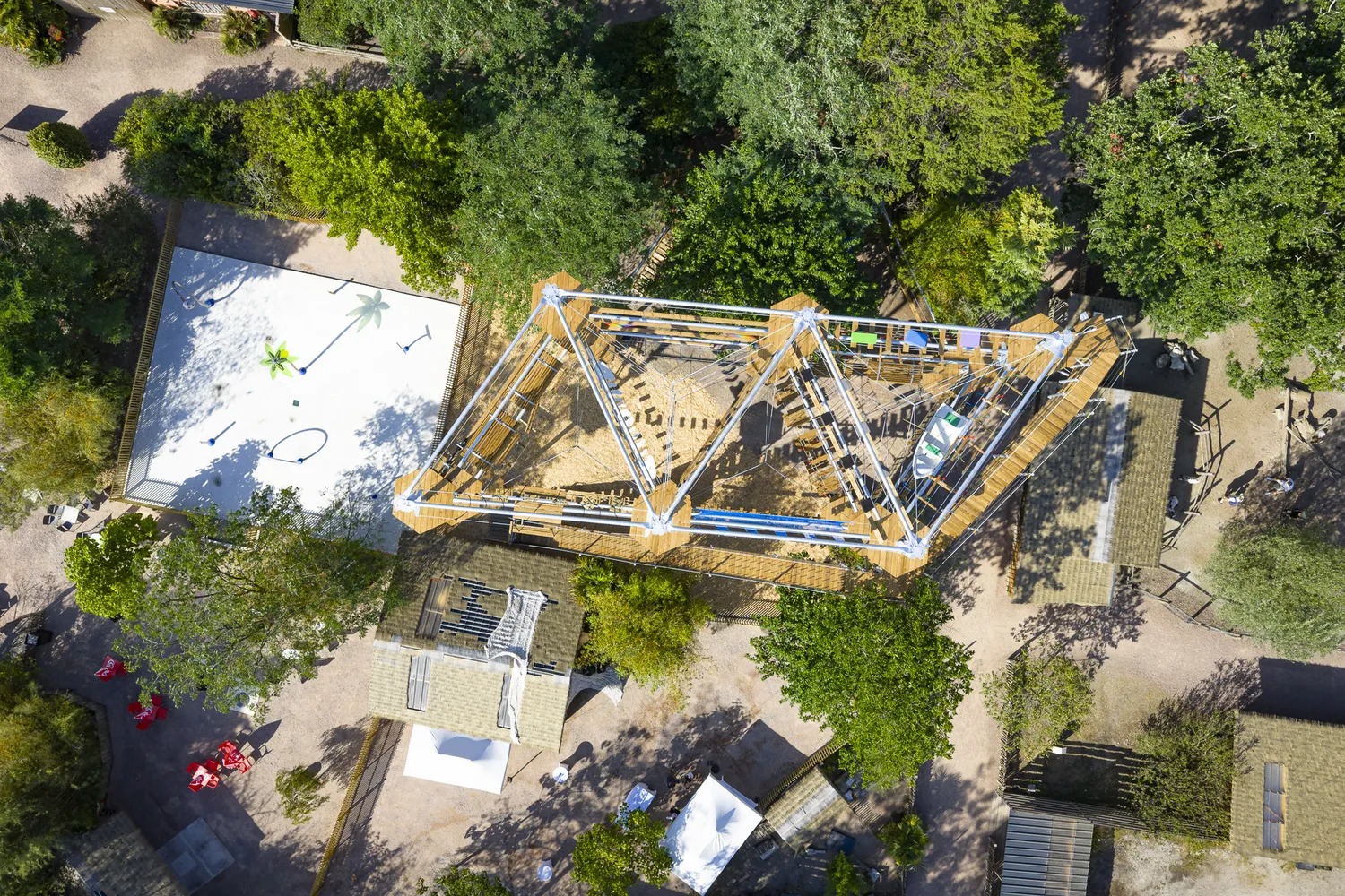Aerial view of a construction site with yellow and blue scaffolding surrounded by greenery and buildings at Les Cimes de Bordeaux in Pessac