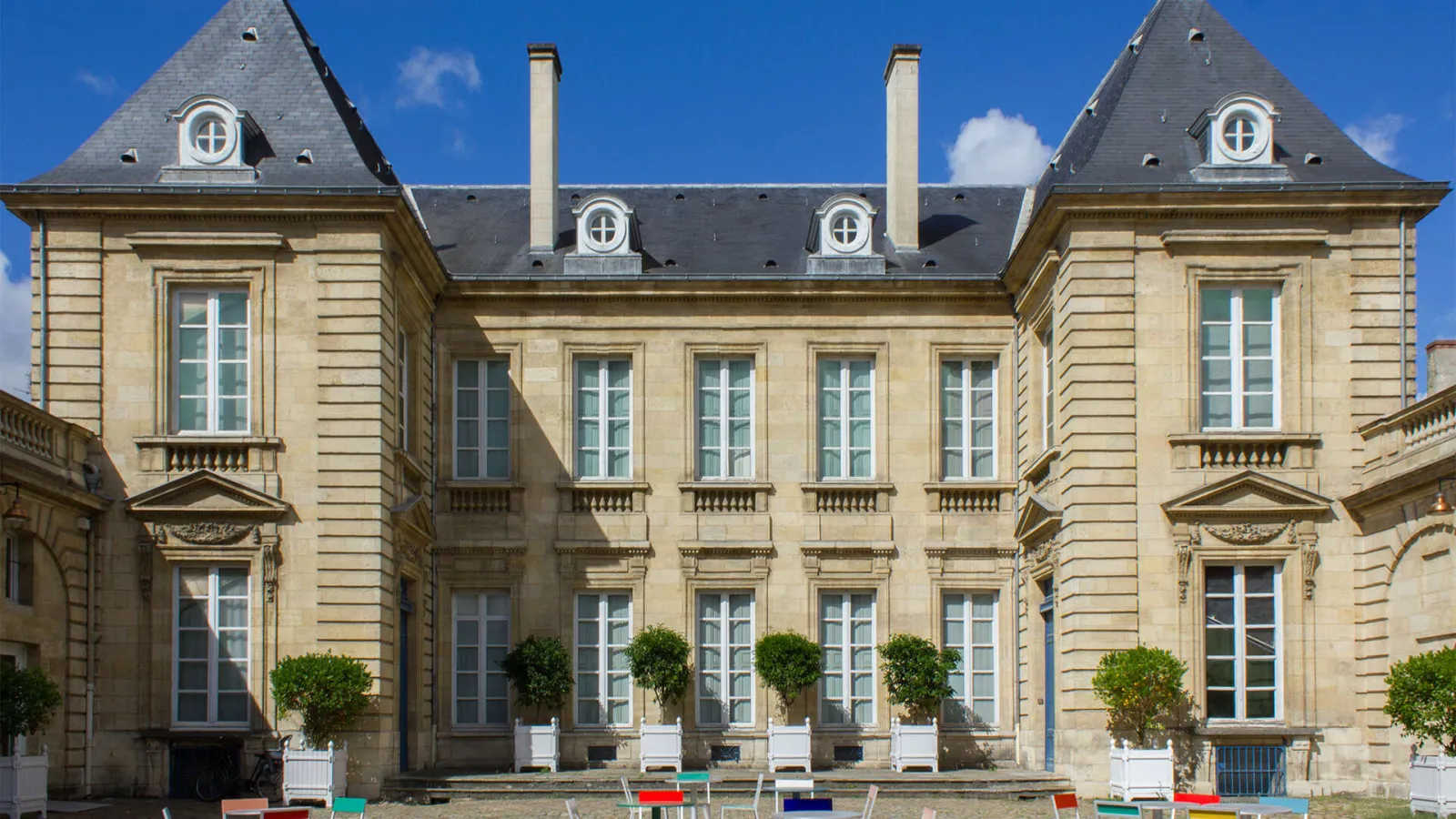 Facade of the Museum of Decorative Arts and Design in Bordeaux, a classical stone building with mansard roofs, mullioned windows and a garden with topiary box shrubs