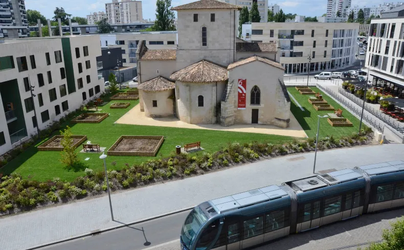 Aerial view of Saint-Vincent Church surrounded by modern residential buildings, with a tram in the foreground and landscaped gardens in Mérignac, Bordeaux.