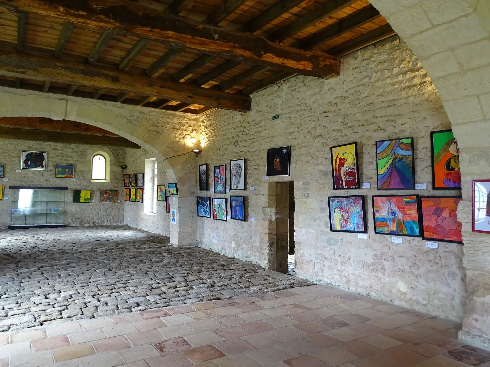 Interior of an art gallery in a fortress featuring stone walls, exposed wooden beams, and colorful artworks displayed on the walls.