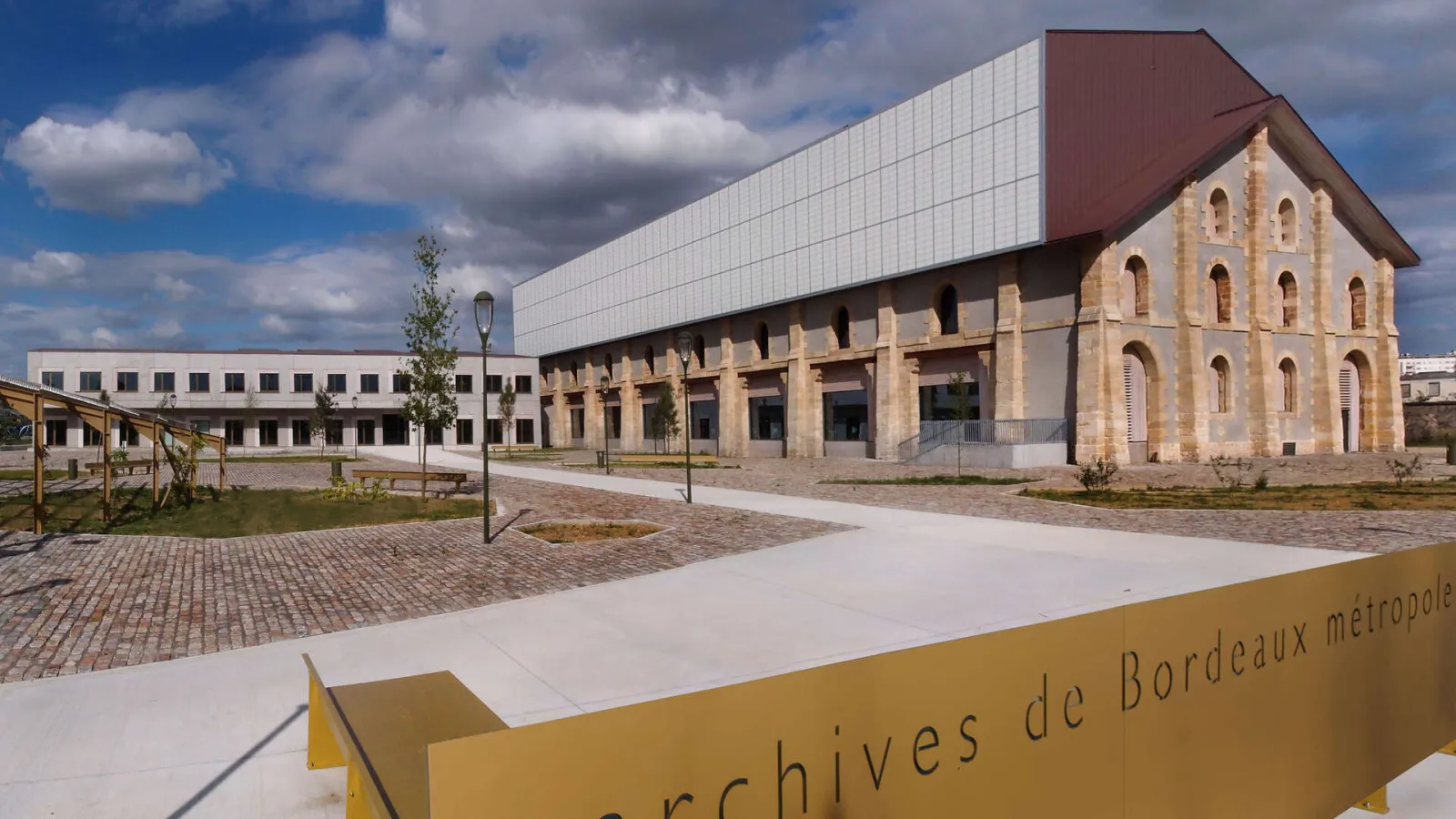 Modern Archives of Bordeaux Métropole building featuring a stone facade and contemporary roofing, surrounded by a paved courtyard and green spaces.