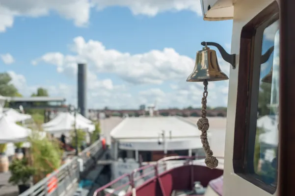 Brass bell hanging at a window overlooking the Garonne River and Bordeaux waterfront