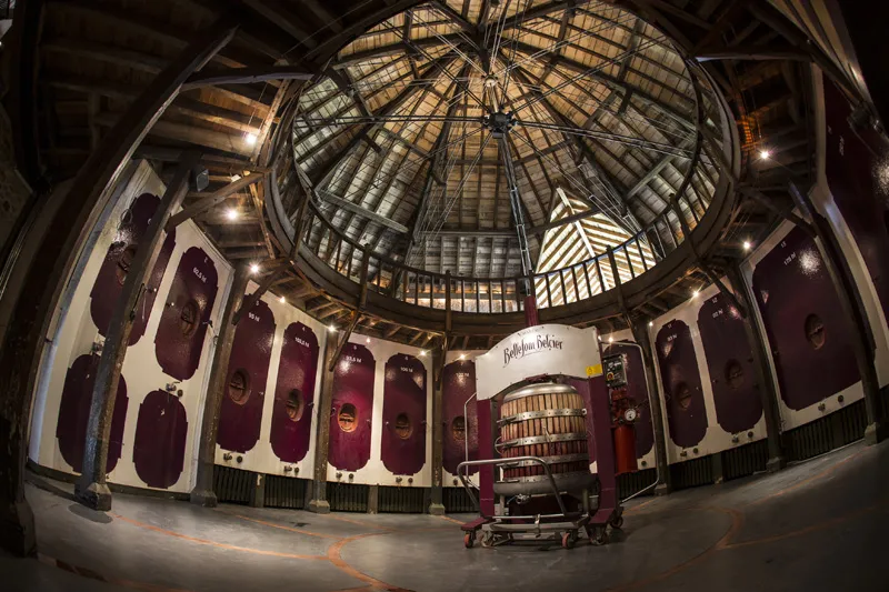 Interior of Château Bellefont Belcier in Bordeaux: large circular room with glass dome ceiling, burgundy arched doors, and wine tasting furniture.