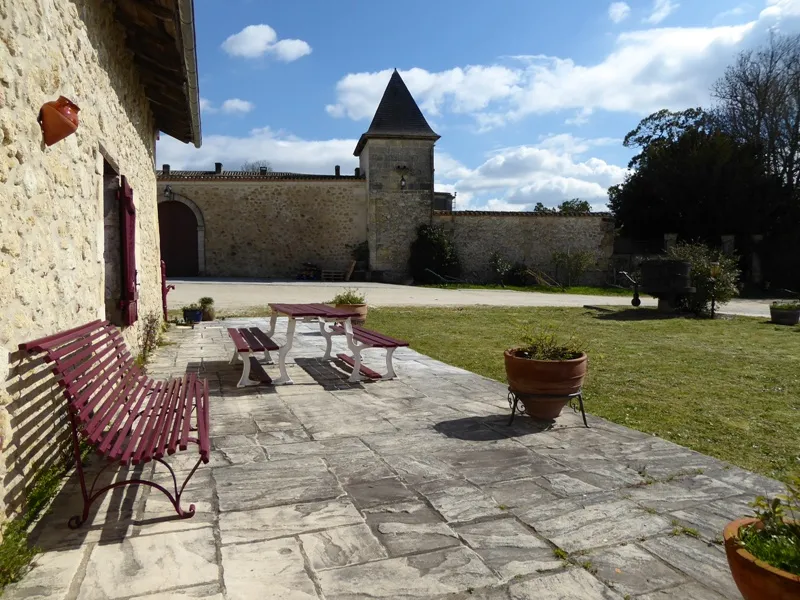 Inner courtyard of Château de Lisennes in Bordeaux featuring red benches, picnic table, stone walls and central tower under blue sky