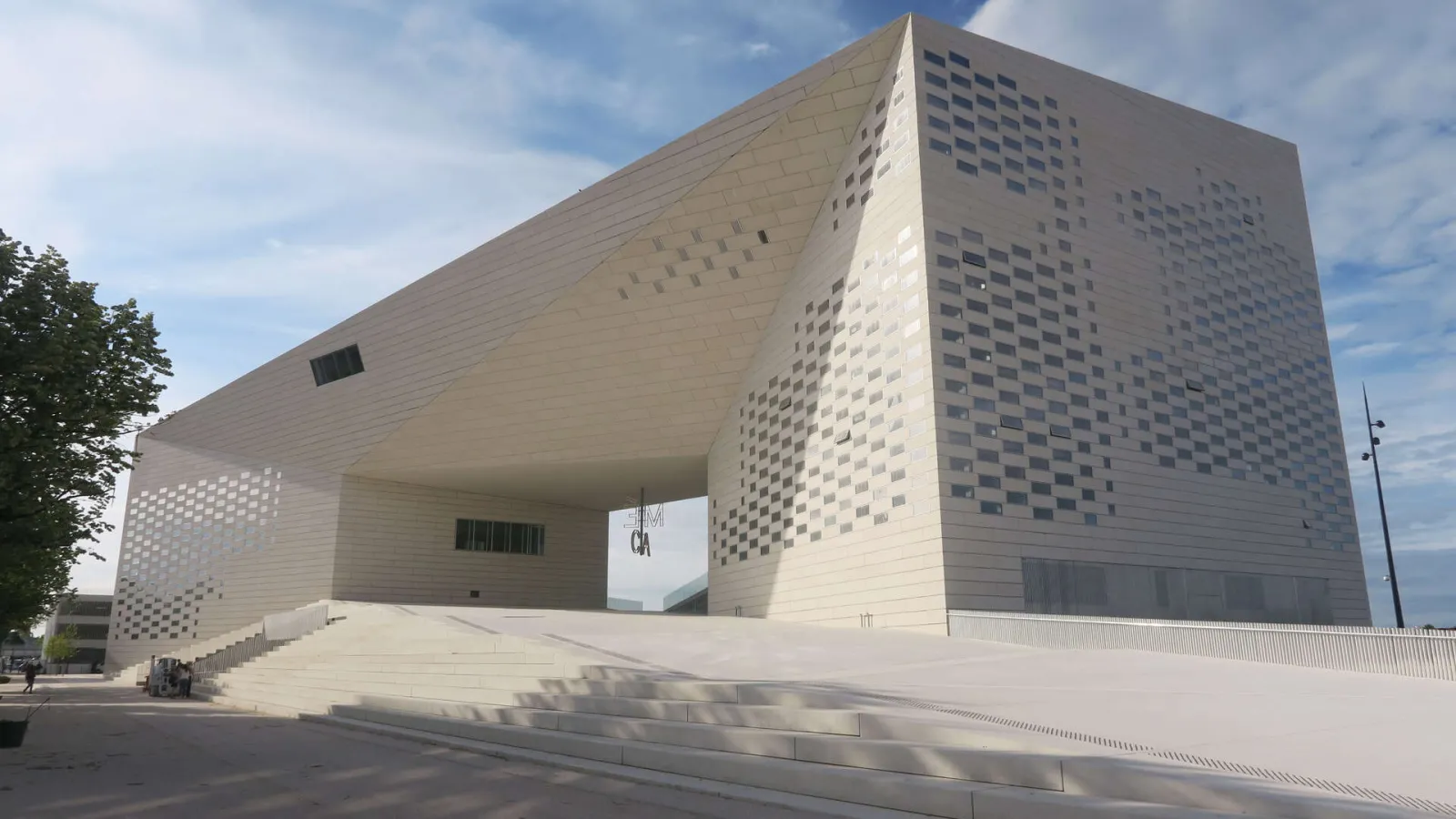 Modern white stone building of La Méca in Bordeaux featuring a distinctive perforated facade and entrance stairs, headquarters of the House of Creative and Cultural Economy in Nouvelle-Aquitaine.