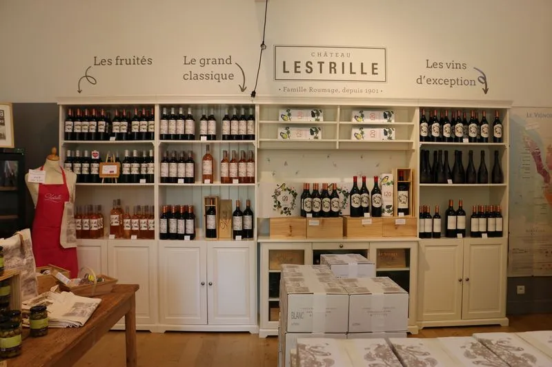 Interior of Château Lestrille shop in Bordeaux displaying shelves with wines, fruits, and classic products, with signs categorizing the different product sections.