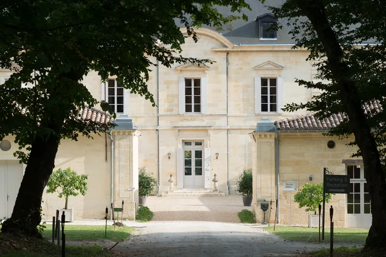 Main facade of Château Siaurac in Bordeaux, a neoclassical stone building with mansard roof, framed by tall trees, featuring a columned portico entrance.