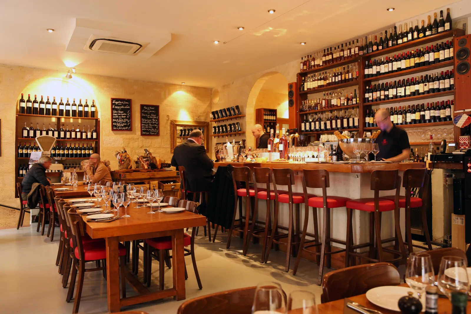 Elegant interior of a Bordeaux brasserie featuring a wooden bar, wine bottle shelves, dining tables with seated guests, and warm golden décor.