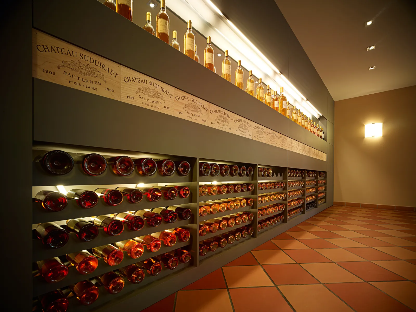 Tasting cellar of Château Suduiraut in Bordeaux showcasing vintage bottles of Sauternes displayed in illuminated alcoves, with historical estate labels in the background.