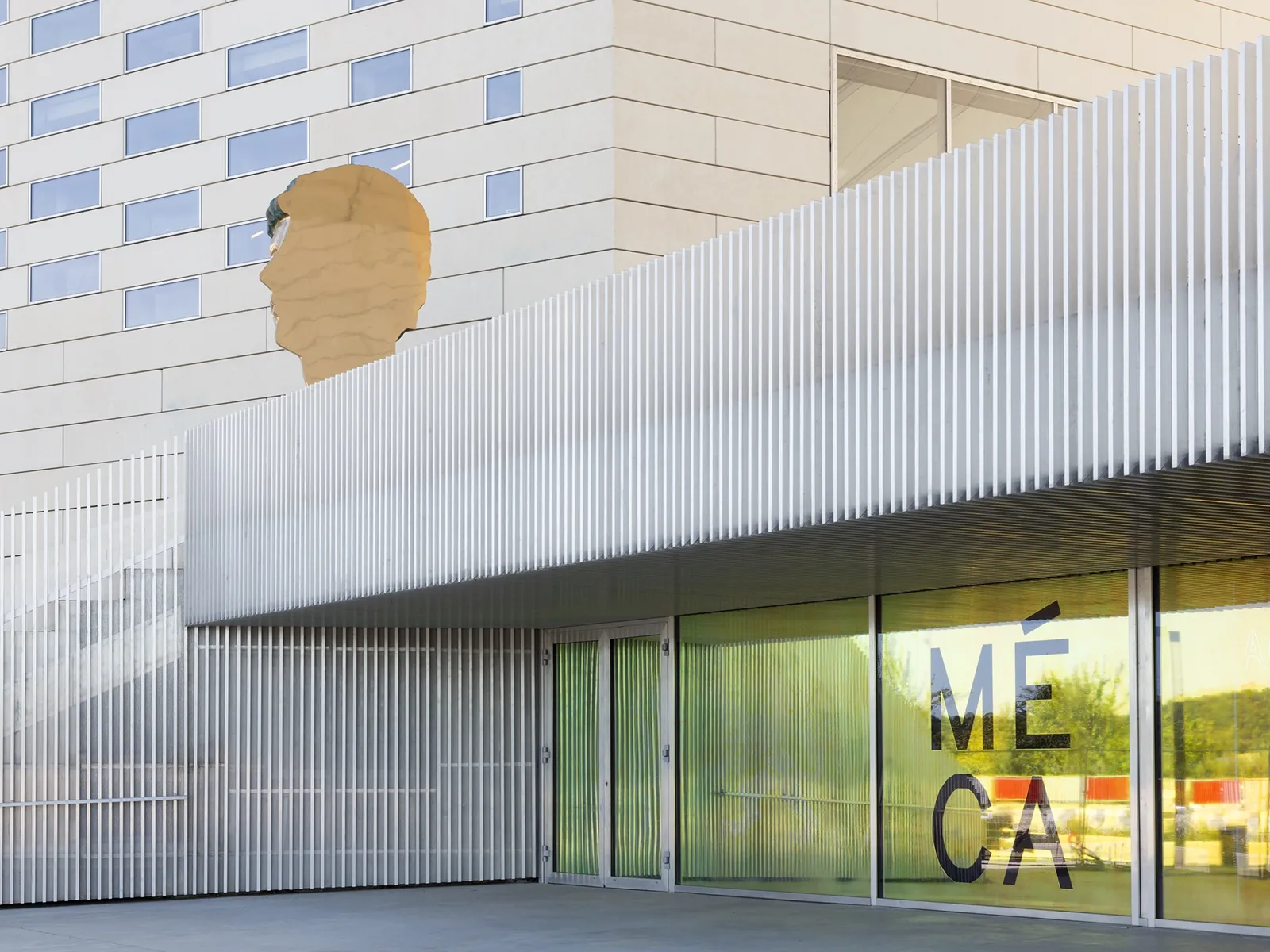 Exterior view of FRAC Nouvelle-Aquitaine MECA in Bordeaux featuring a large sculptural portrait relief on a white metal wall panel and a green storefront window with the museum name.