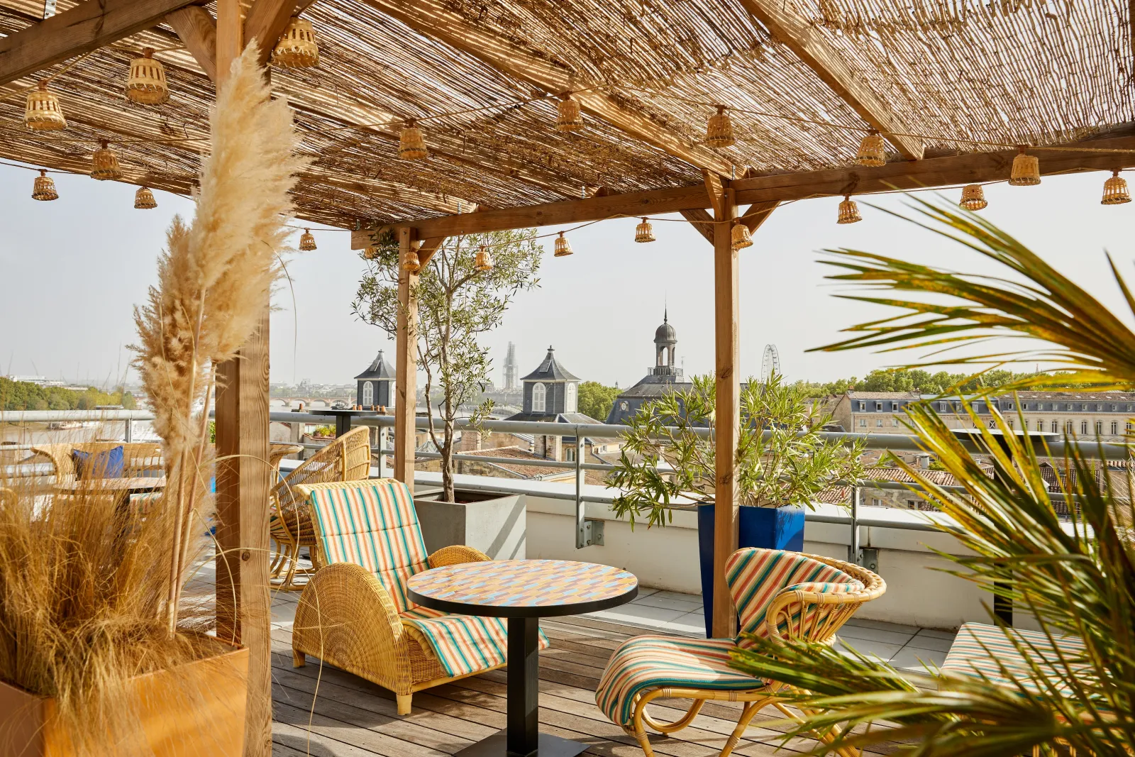 Covered terrace at Indigo Hotel Bordeaux featuring striped loungers and panoramic views of Bordeaux rooftops and church spires