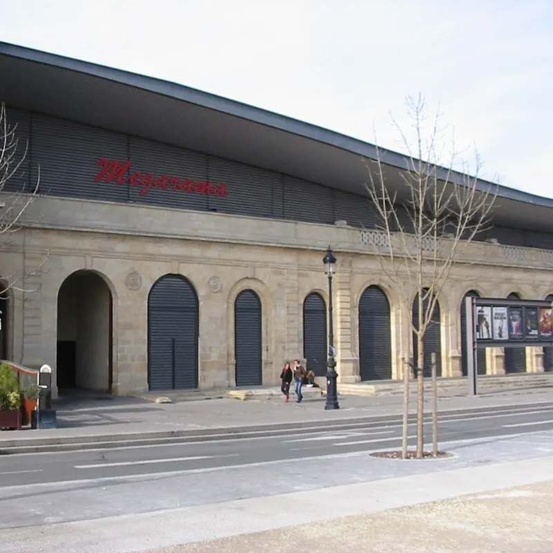 Exterior view of Mégarama Bordeaux Bastide cinema featuring modern architecture with arched doors and a red sign, located in Bordeaux.