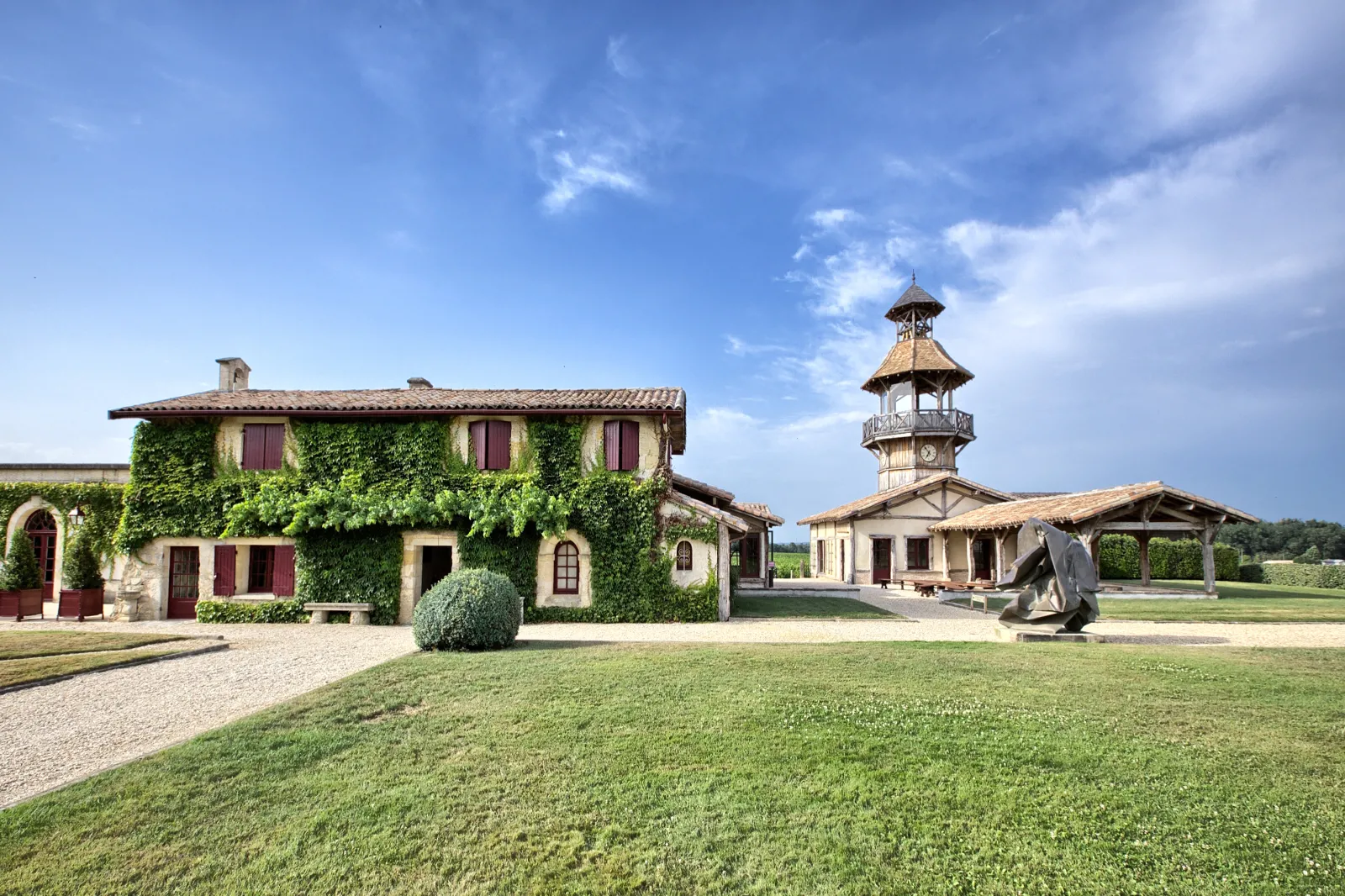 Exterior view of Château Smith Haut Lafitte in Bordeaux featuring ivy-covered main building, clock tower, manicured lawn and clear blue sky