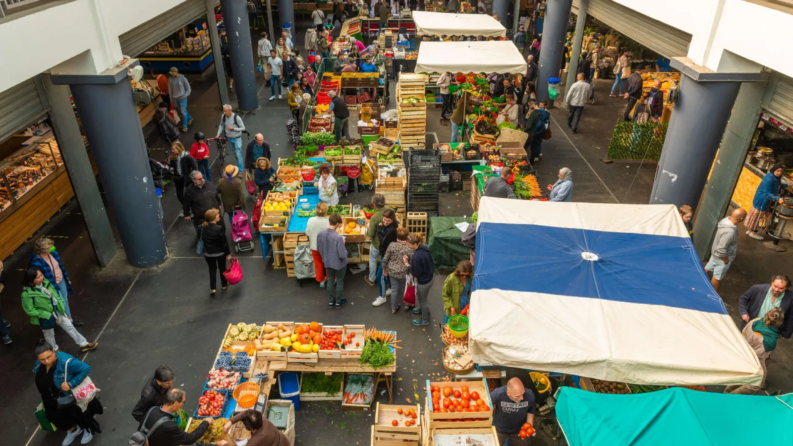 Overhead view of Capucins Market in Bordeaux featuring produce stalls, shoppers and vendors under white and blue umbrellas