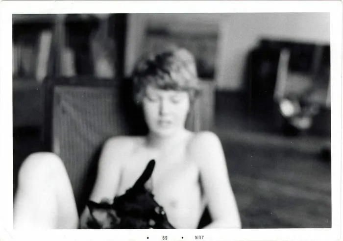 Black and white photograph of a seated woman wearing a sleeveless garment in a blurred interior setting. Digitized archival image dated 1969.