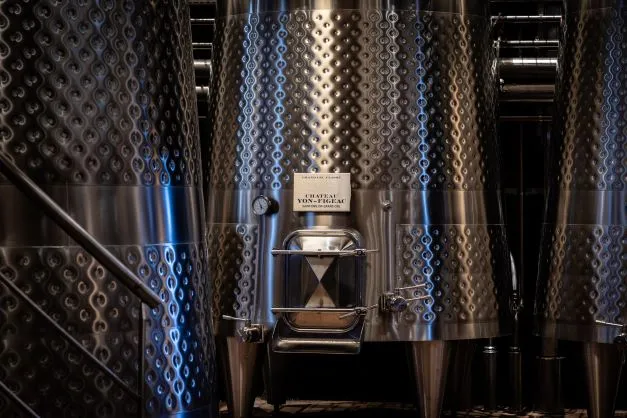 Stainless steel fermentation tanks with geometric patterns at Château Yon-Figeac in Bordeaux, featuring a wine label on the central tank