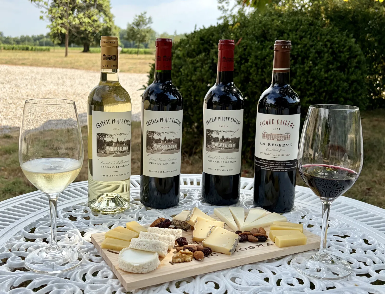 Wine tasting from Château Picque Caillou featuring white and red wines with cheese and nuts selection on a white table in Bordeaux vineyards.