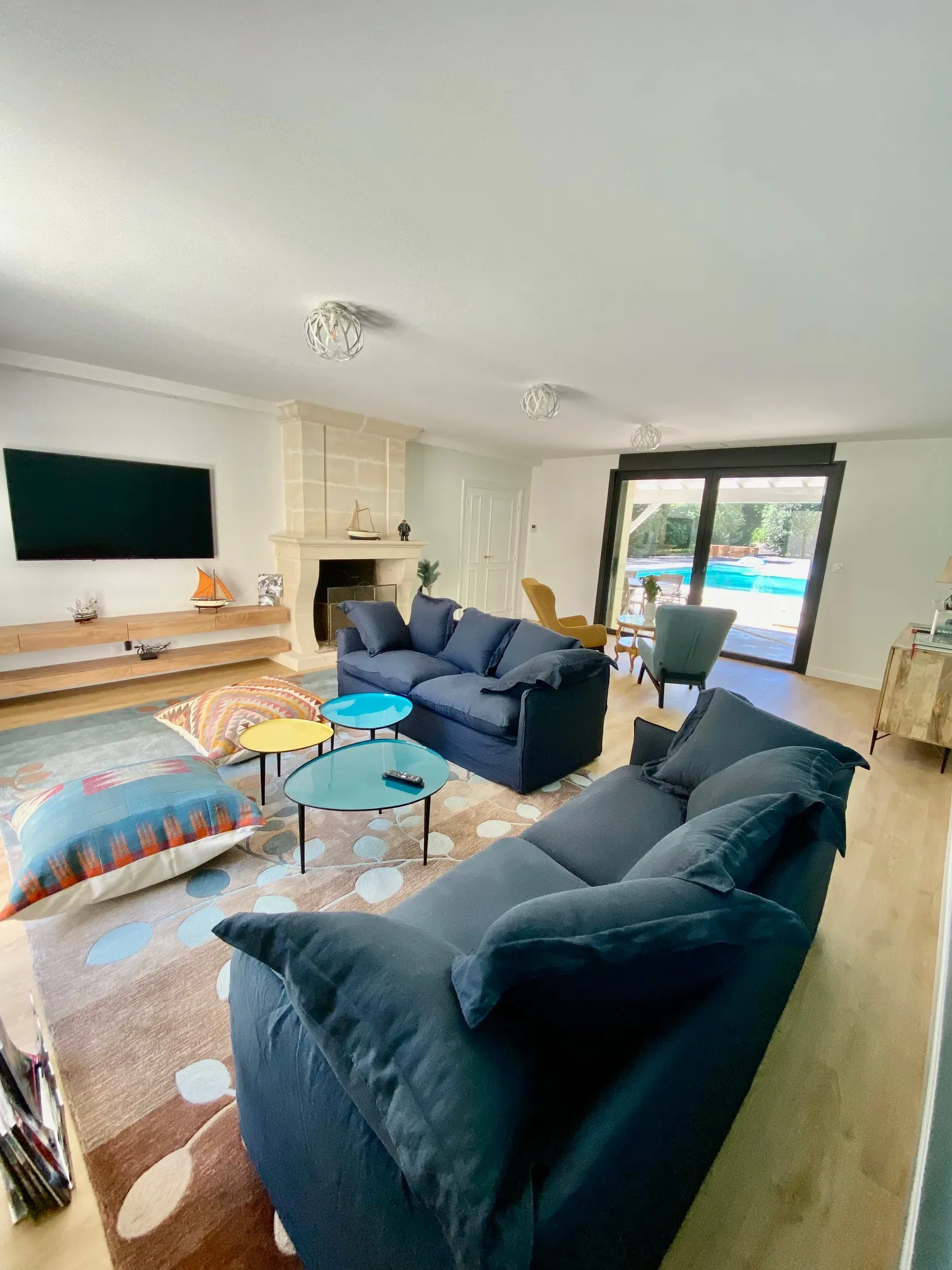 Spacious living room with two navy blue sofas, coffee tables, fireplace, wall-mounted TV and access to a terrace with swimming pool in Bordeaux.