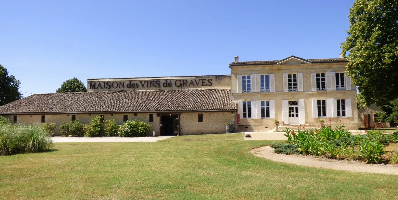 Facade of the Maison des Vins de Graves in Bordeaux, a stone building with tiled roof, surrounded by gardens and lawn.