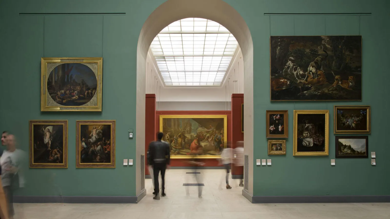 Gallery in the Bordeaux Museum of Fine Arts featuring mint green walls, classical paintings in gilt and red frames, central archway with skylight, visitors viewing the artworks