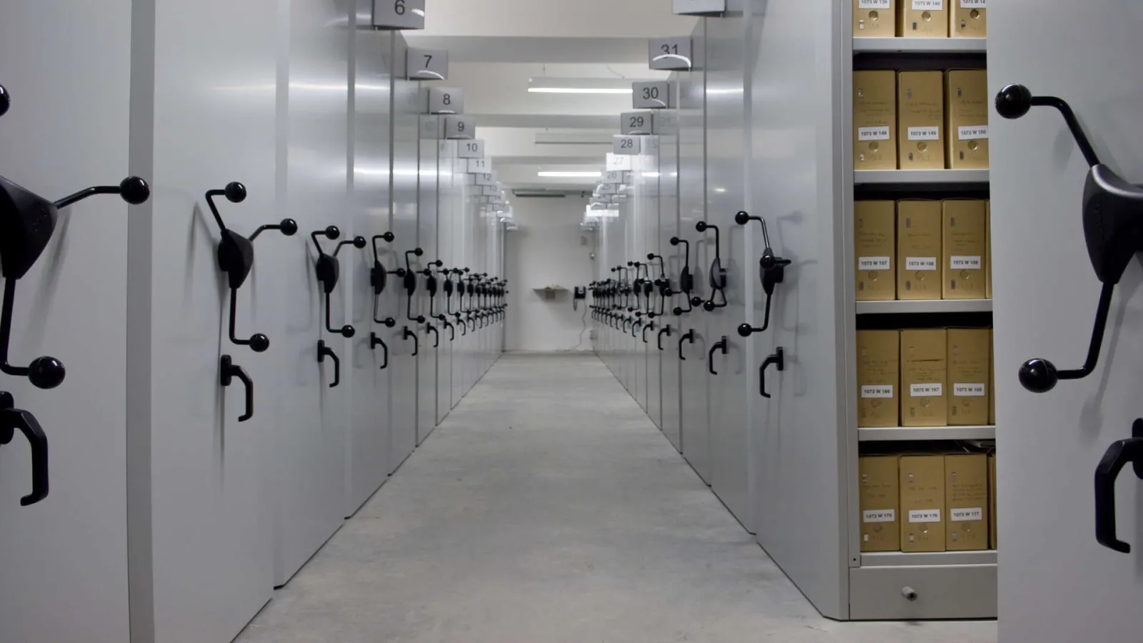 Archive corridor at Bordeaux Métropole with numbered storage boxes arranged in rows on both sides and filing cabinets on the right