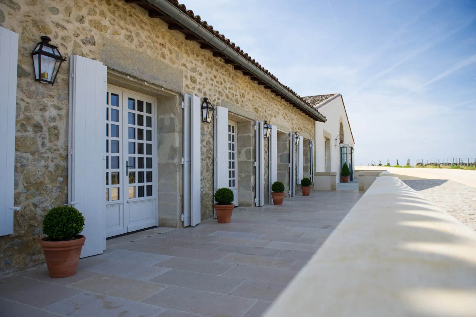 Stone facade of Château de Rayne Vigneau with paved terrace, white paneled doors and boxwood planters, in Bordeaux