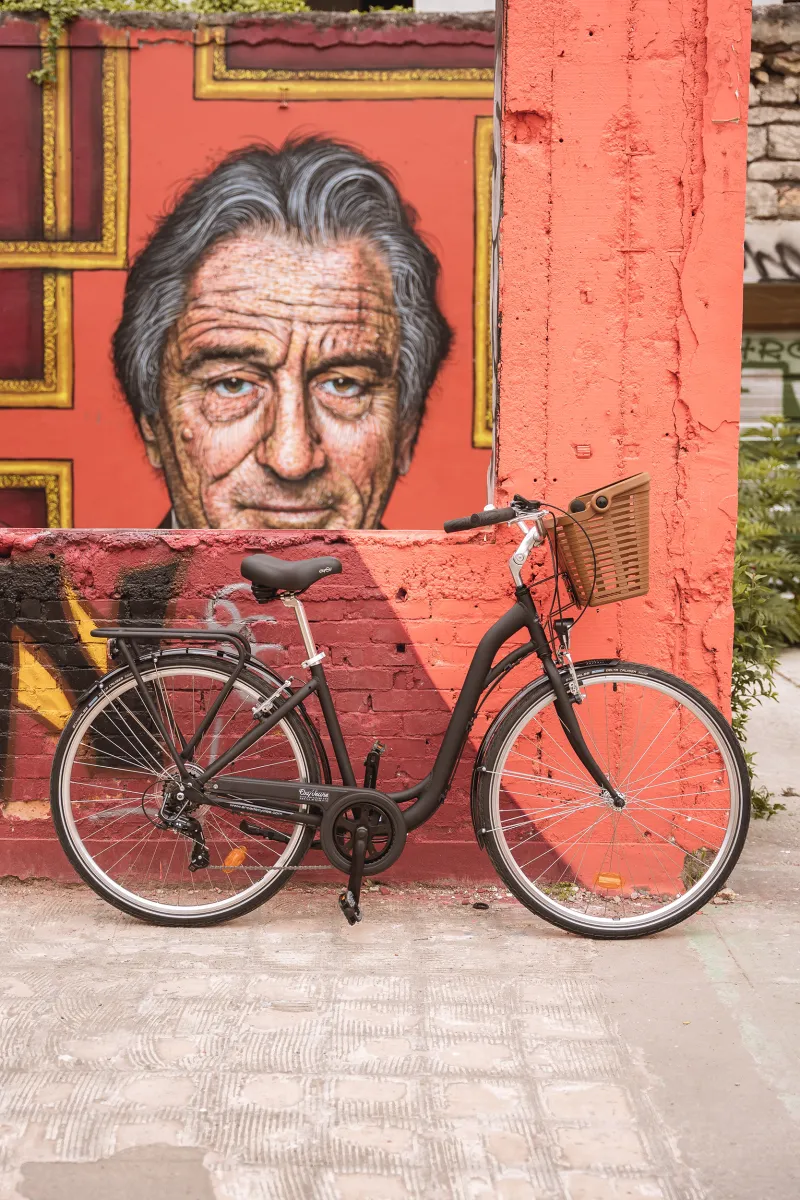 Red bicycle parked in front of a colorful mural depicting a man's portrait in Bordeaux