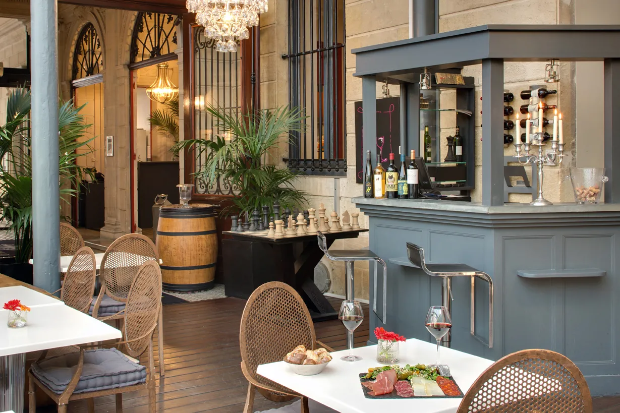 Sophisticated bar and restaurant featuring set tables, rattan chairs, blue-gray counter, chessboard, wine barrels and upscale decor in Bordeaux