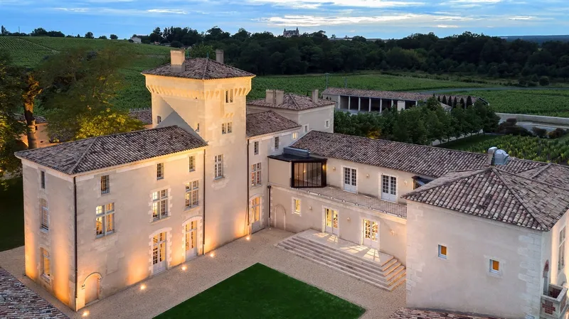 Aerial nighttime view of Château Lafaurie Peyraguey in Bordeaux, illuminated with its distinctive tower, tiled roofs and terraces, surrounded by vineyards.