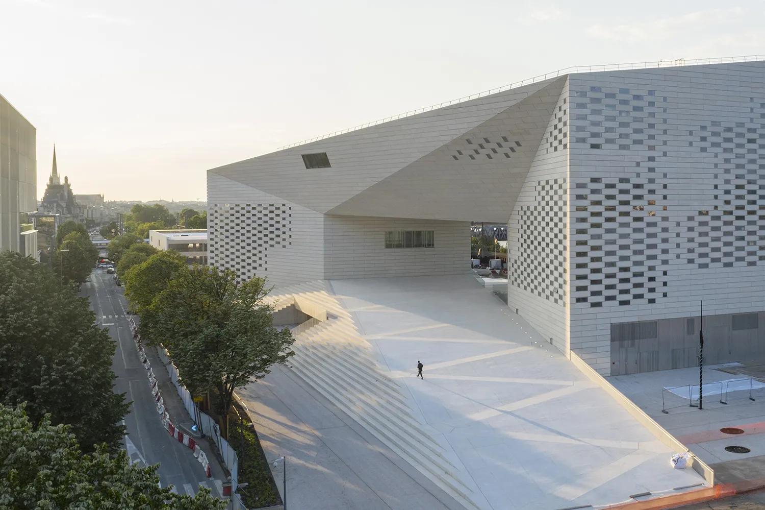Exterior view of FRAC Nouvelle-Aquitaine MECA in Bordeaux, modern white building with perforated checkerboard facade, access stairs and large plaza, church visible in background