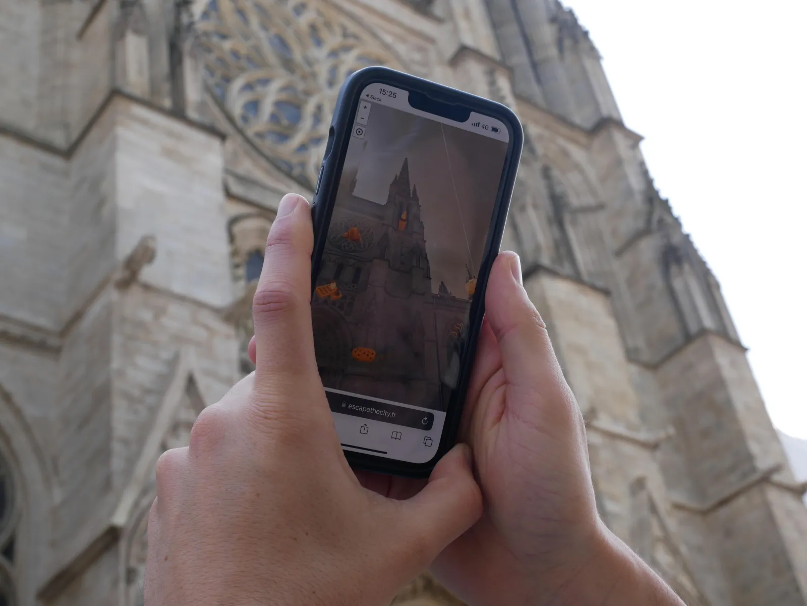 Hand holding a smartphone displaying an augmented reality app showing an orange-lit church, with Bordeaux cathedral in the background