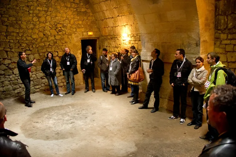 Group of badge-wearing visitors listening to a guide in the vaulted underground passages of Blaye Citadel, with stone walls lit by warm lighting.