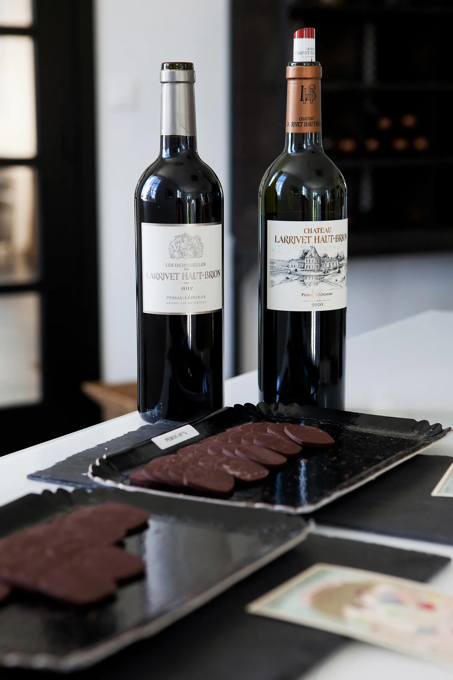 Two red wine bottles from Château Larrivet Haut-Brion displayed on a black table with sliced charcuterie in an elegant setting