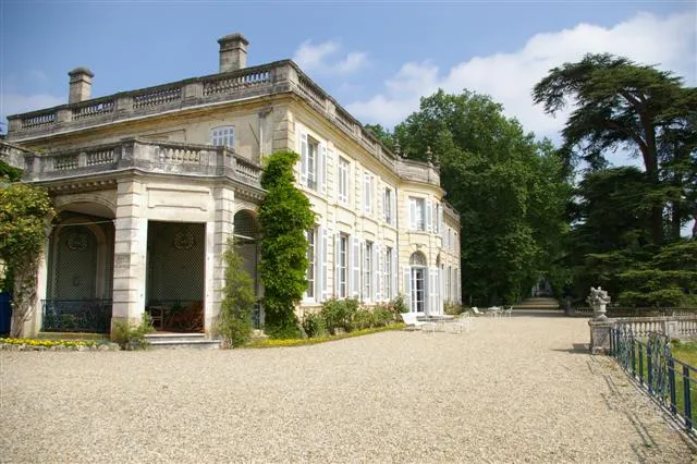 Château du Taillan in Bordeaux, an elegant 18th-century manor house featuring a stone façade, columned entrance portico, roof balustrade, surrounded by lush greenery and gravel courtyard.