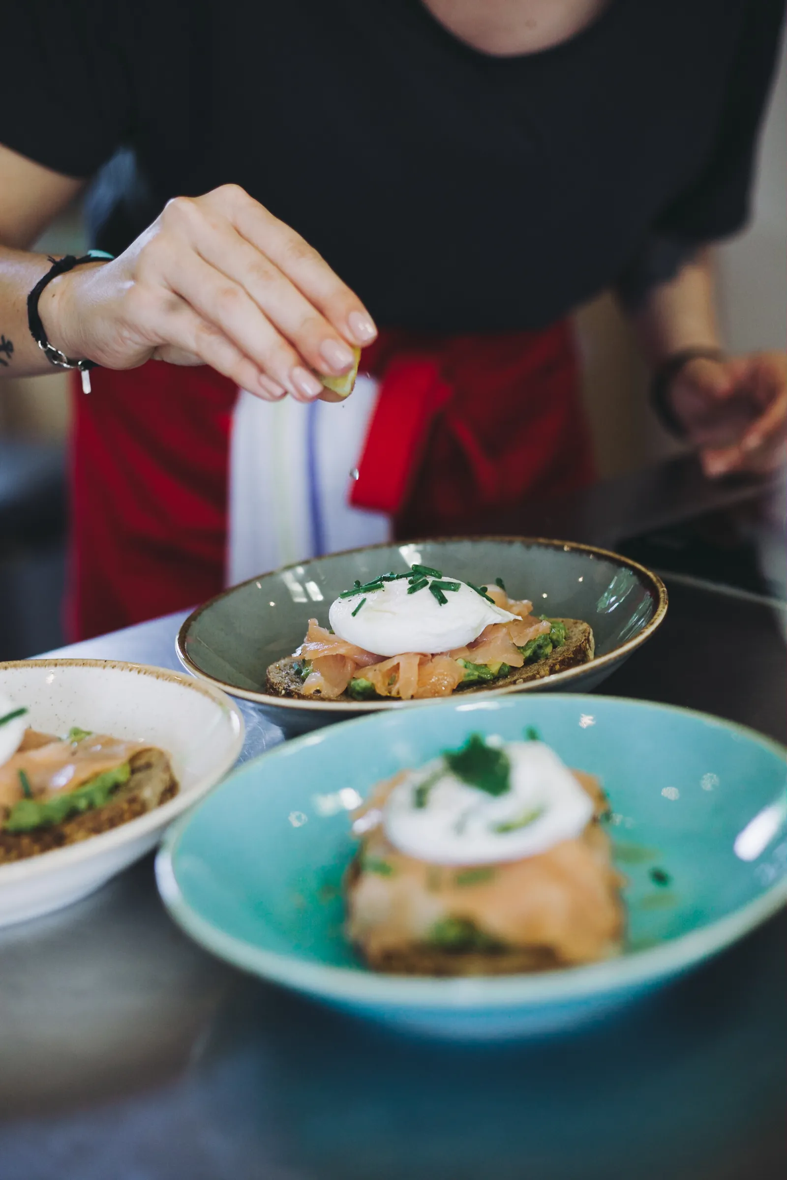 A person in a black shirt and red pants presents gourmet plates topped with poached eggs and green vegetables at Château Ambe Tour Pourret in Bordeaux.