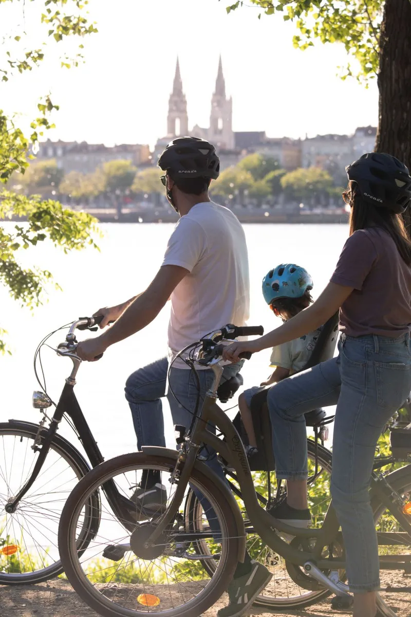 Family cycling in front of the Saint-Michel Basilica in Bordeaux, overlooking the Garonne river and leafy trees