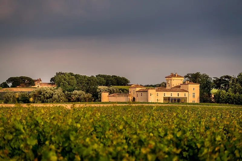 Château Lafaurie Peyraguey, an ochre-colored Bordeaux estate surrounded by lush vineyards in the wine region of Bordeaux.