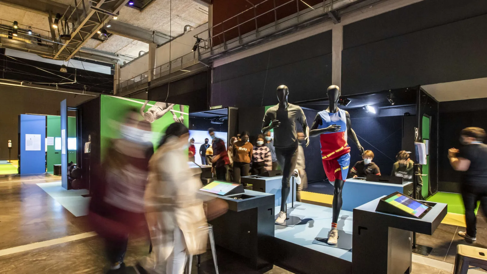 Interactive sports exhibition at Cap Sciences Bordeaux featuring running mannequins, touchscreen displays, and visitors exploring the modern exhibition space.