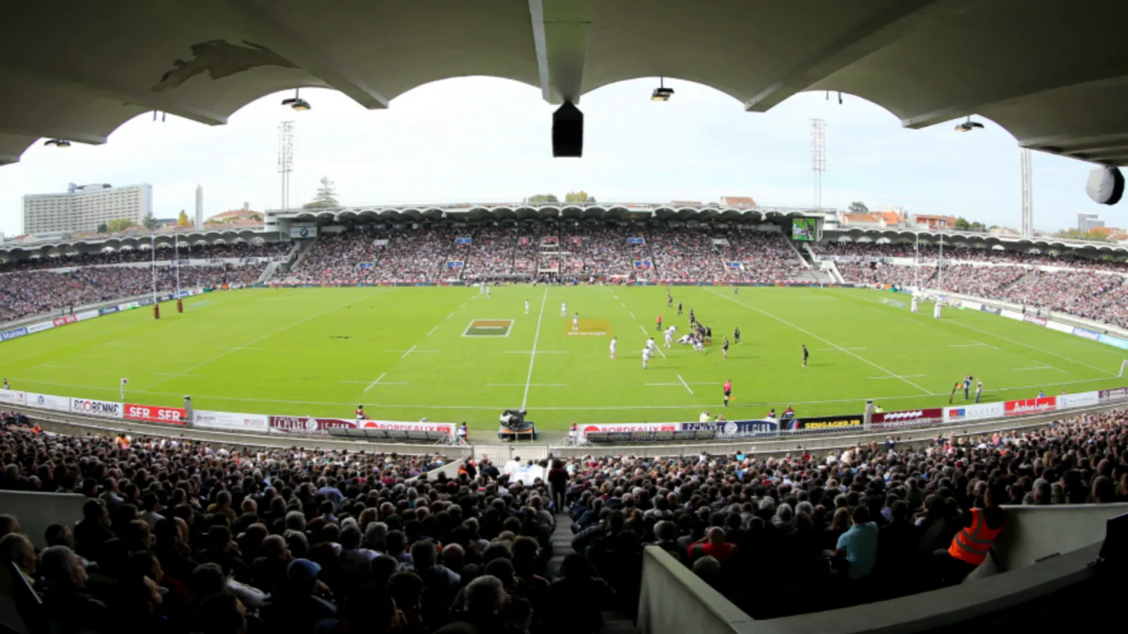Panoramic view of Stade Chaban-Delmas in Bordeaux during a rugby match, with crowded stands and the playing field in the foreground.