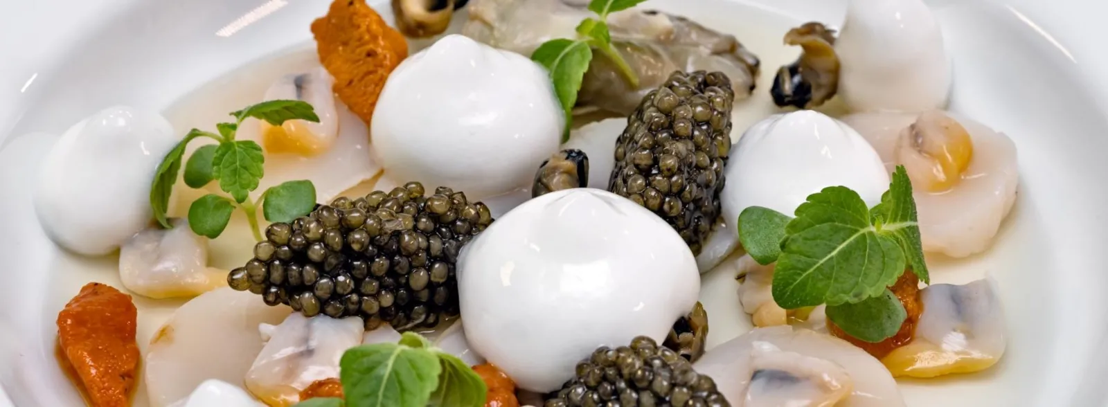 Gourmet plate from Saint-James in Bordeaux featuring fish roe, caviar pearls, white quenelles, citrus segments and fresh herbs on white background