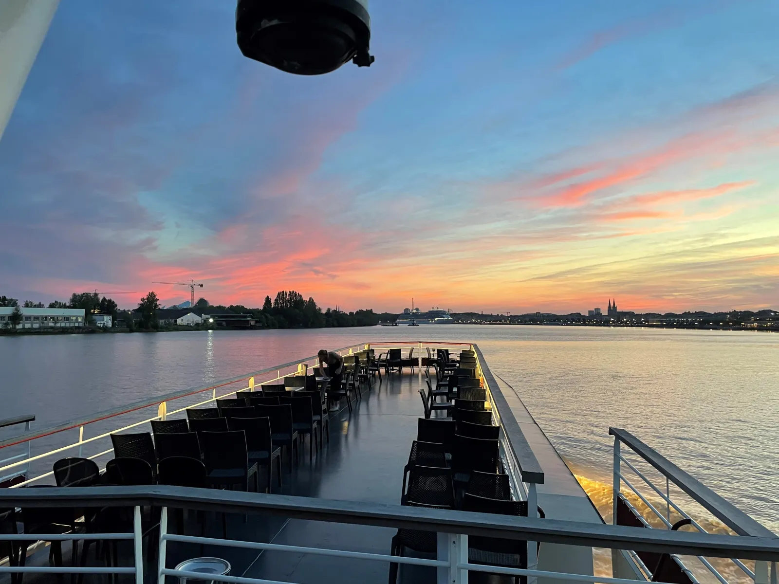 Upper deck of the Maddalena yacht in Bordeaux at sunset, featuring rows of black chairs, the Garonne river and the city skyline in the background.