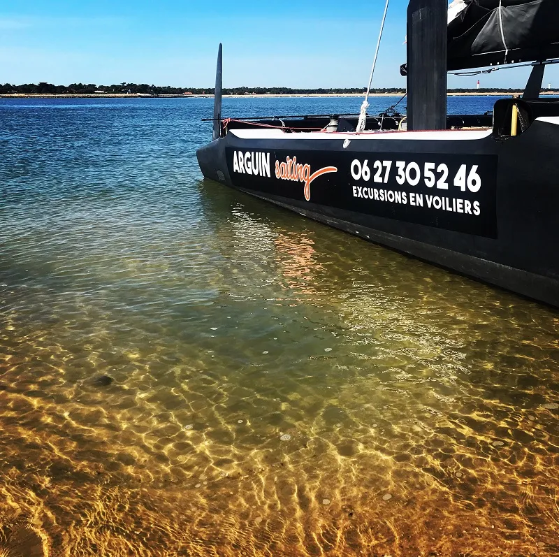 Black Arguin Sailing boat moored in the crystal-clear waters of Bordeaux, displaying contact information and offering sailing excursions.