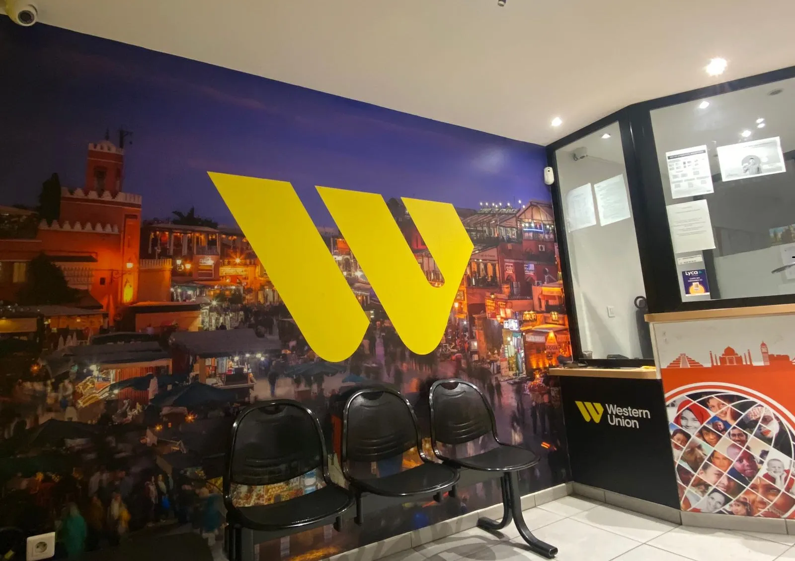 Western Union branch in Bordeaux featuring large yellow logo on wall, black chairs, Gambetta square display and illuminated Bordeaux cityscape