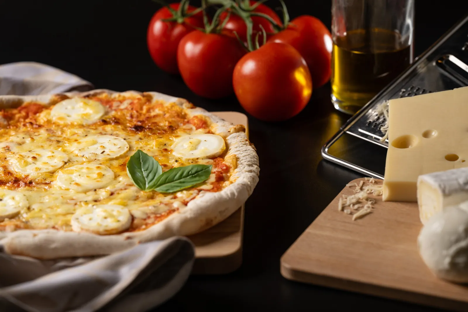 Margherita pizza topped with mozzarella and fresh basil, served with cherry tomatoes, olive oil and cheese on a black table