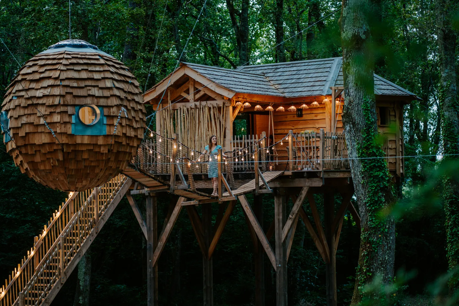 Girondine treehouses in Bordeaux: wooden structures with shingled roofs, connecting walkway and elevated platform nestled in the forest